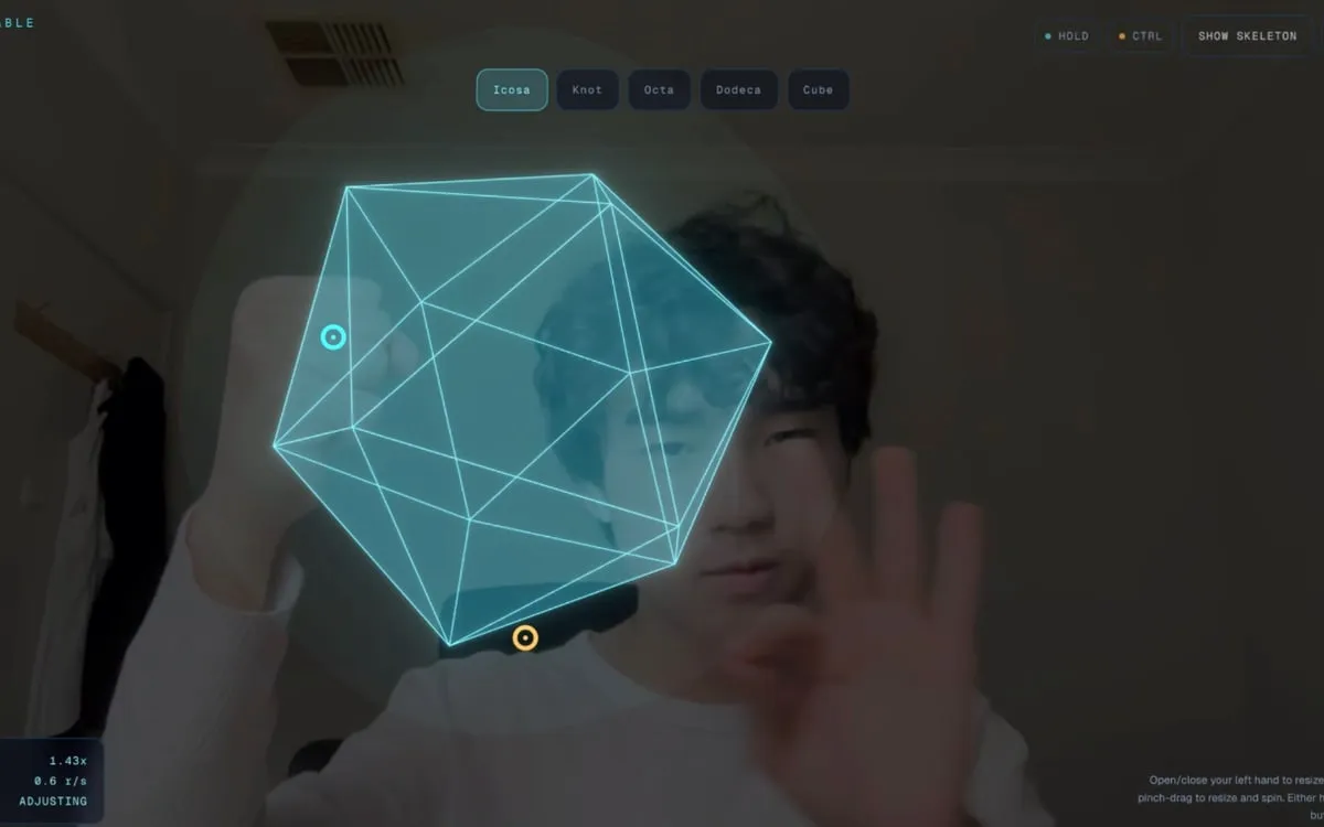 Screenshot of HoloTable showing a glowing cyan wireframe icosahedron floating above an open palm in a live webcam feed, rendered in the browser